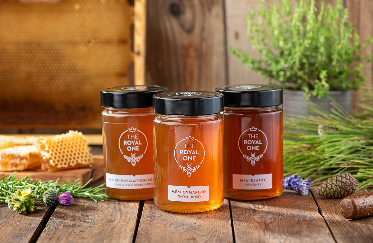 Packaging and label design for the royal one greek honey. Σχεδιασμός συσκευασίας και ετικέτας. Η συσκευασία ακολουθεί μια σύγχρονη εικαστική προσέγγιση, λιτή αλλά “φρέσκια”. Ένα sleeve αγκαλιάζει το βάζο με το μέλι και κάνει το προϊόν ευδιάκριτο στο ράφι. Ταυτόχρονα από τα πλάγια της συσκευασίας ο καταναλωτής μπορεί να περιεργαστεί το χρώμα και την ρευστότητα του προϊόντος. Με funky χρωματικό κώδικα peach-πορτοκαλί, φυστικί-πράσινο και μωβ της λεβάντας συμπληρώνεται η ταυτότητα συσκευασίας των τριών ποικιλιών μελιού που παράγονται, το Μέλι Ελάτης, το Μέλι Πεύκου και Άγριων Βοτάνων και το Θυμαρίσιο Μέλι.